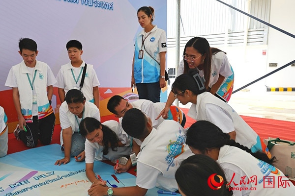 泰國學(xué)生在開營儀式展板上繪制圖案。人民網(wǎng)記者 白元琪攝